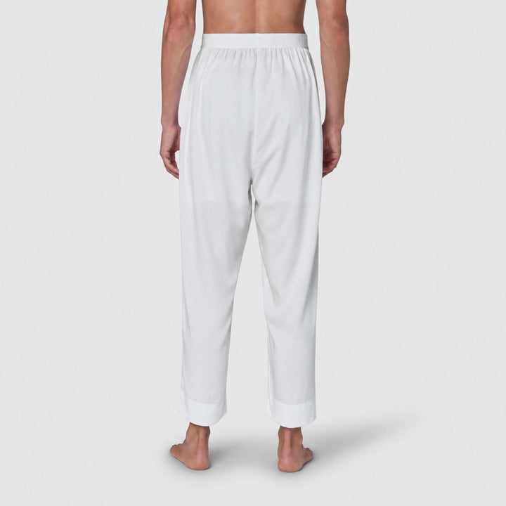 White lounge pants shown from the back on a model, featuring an elastic waistband and relaxed straight-leg fit with rolled cuffs, against a light gray studio background.